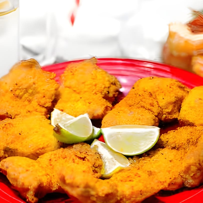 Close-up of crispy, golden-brown chicken wings with lime wedges on a red plate.