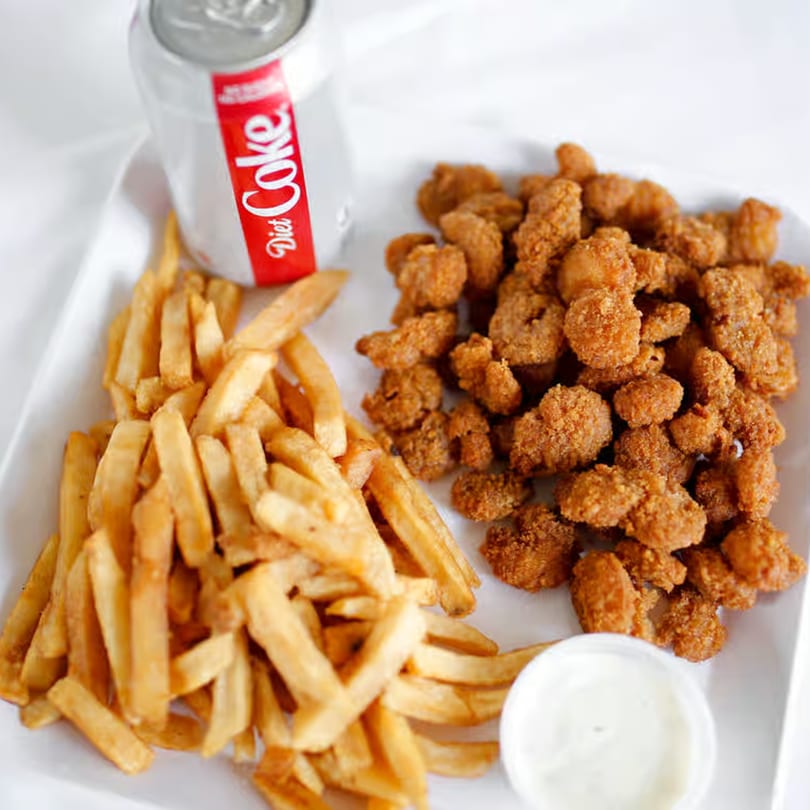 A plate of Buffalo Bill's fried popcorn chicken, french fries, a side of ranch, and a Diet Coke.