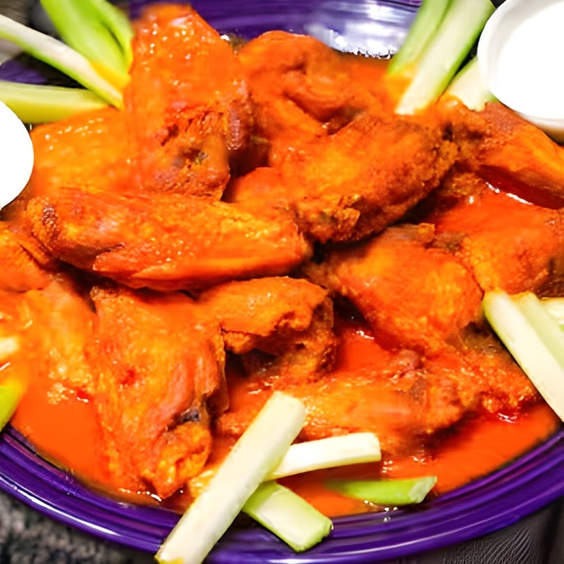 A purple plate piled high with Buffalo Bill's spicy orange wings, celery sticks, and ranch dip.