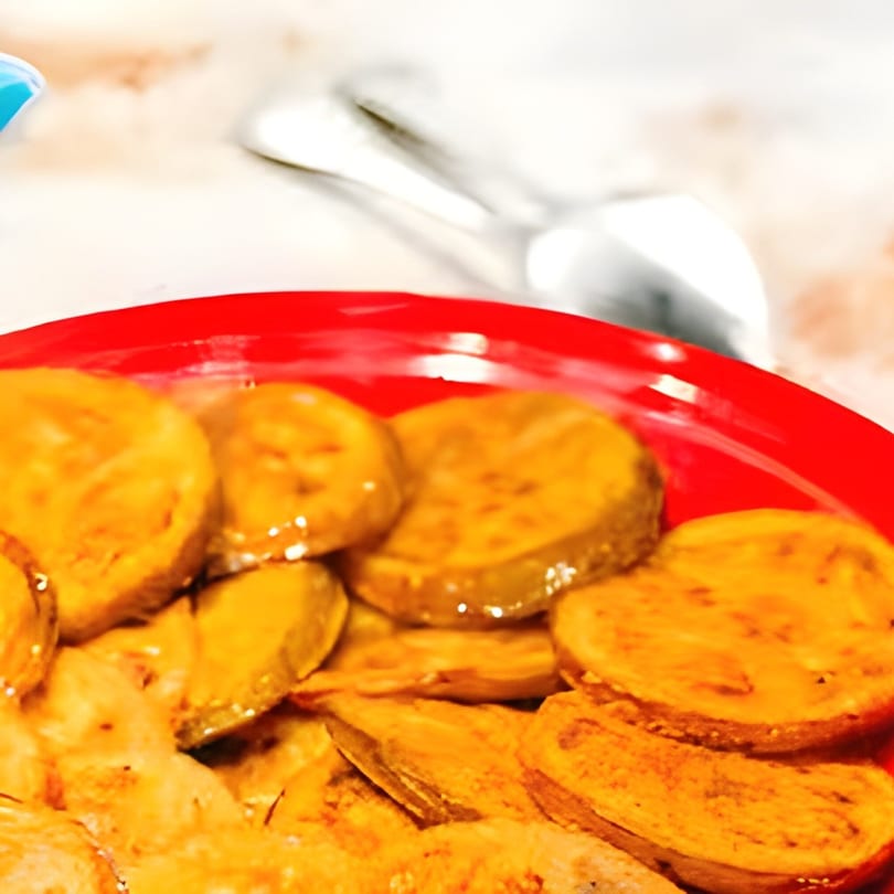 Close-up of golden-brown fried pickles on a red plate, with a serving spoon in the background.